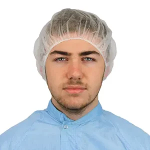 600-3033-Integrity-Bouffant-Style-Pleated-Mob-Caps_V3.webp Cleanroom operative wearing a white pleated flat packed bouffant cap and blue permanent coverall